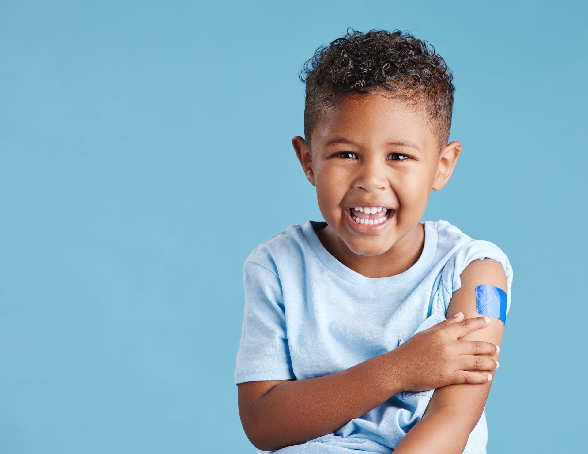 A smiling boy has a bandage on his shoulder where he received a vaccine