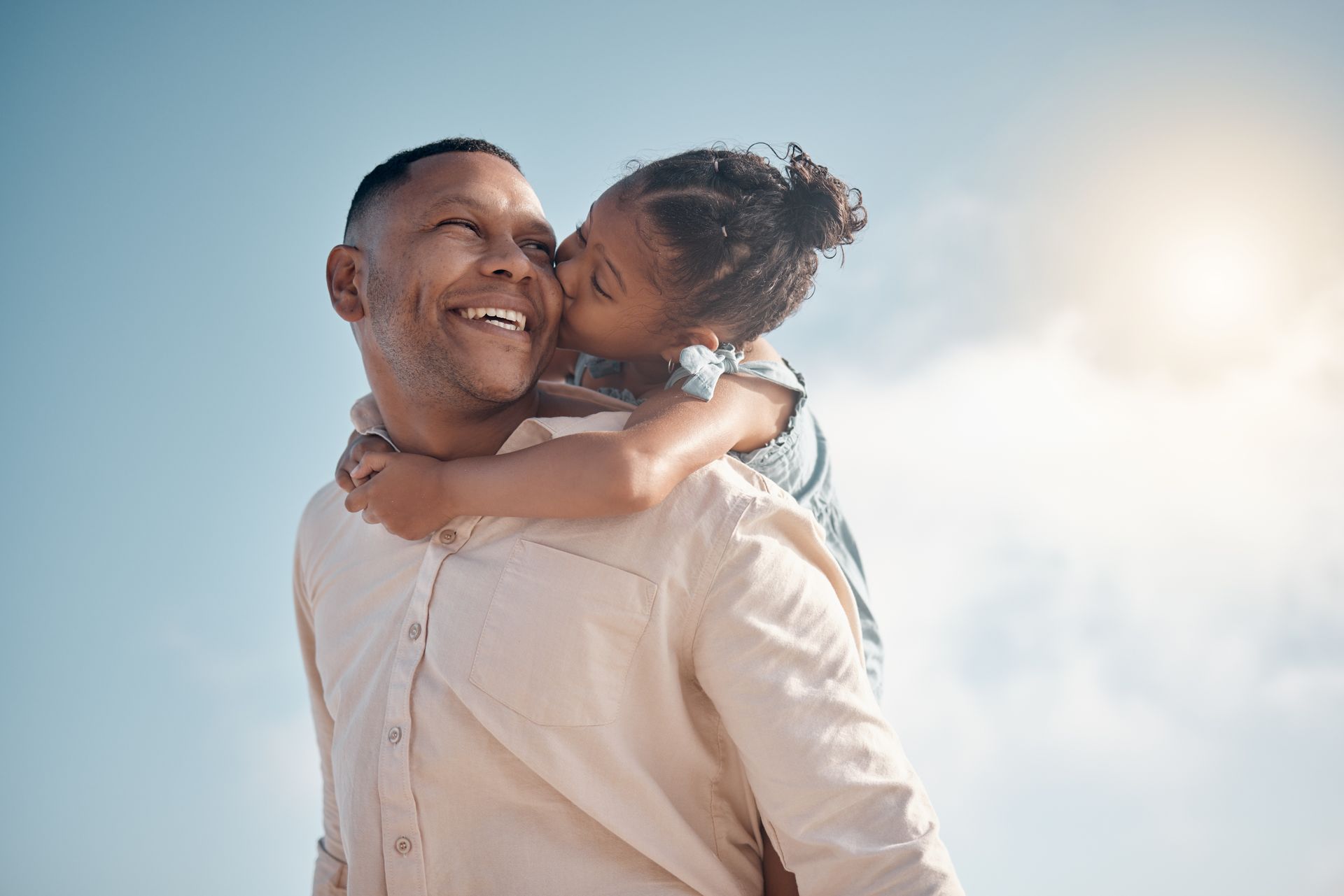 A man is giving a girl and ride on his back while she kisses his check