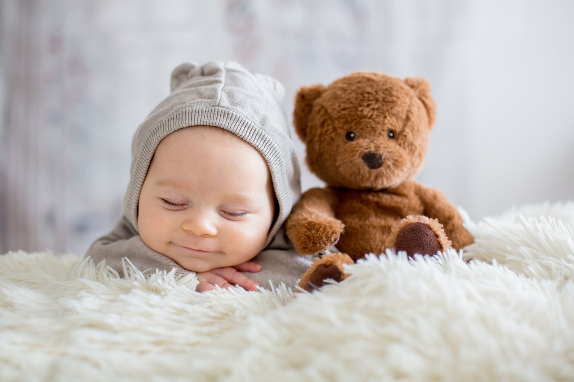 A sleeping baby is smiling with a teddy bear nearby