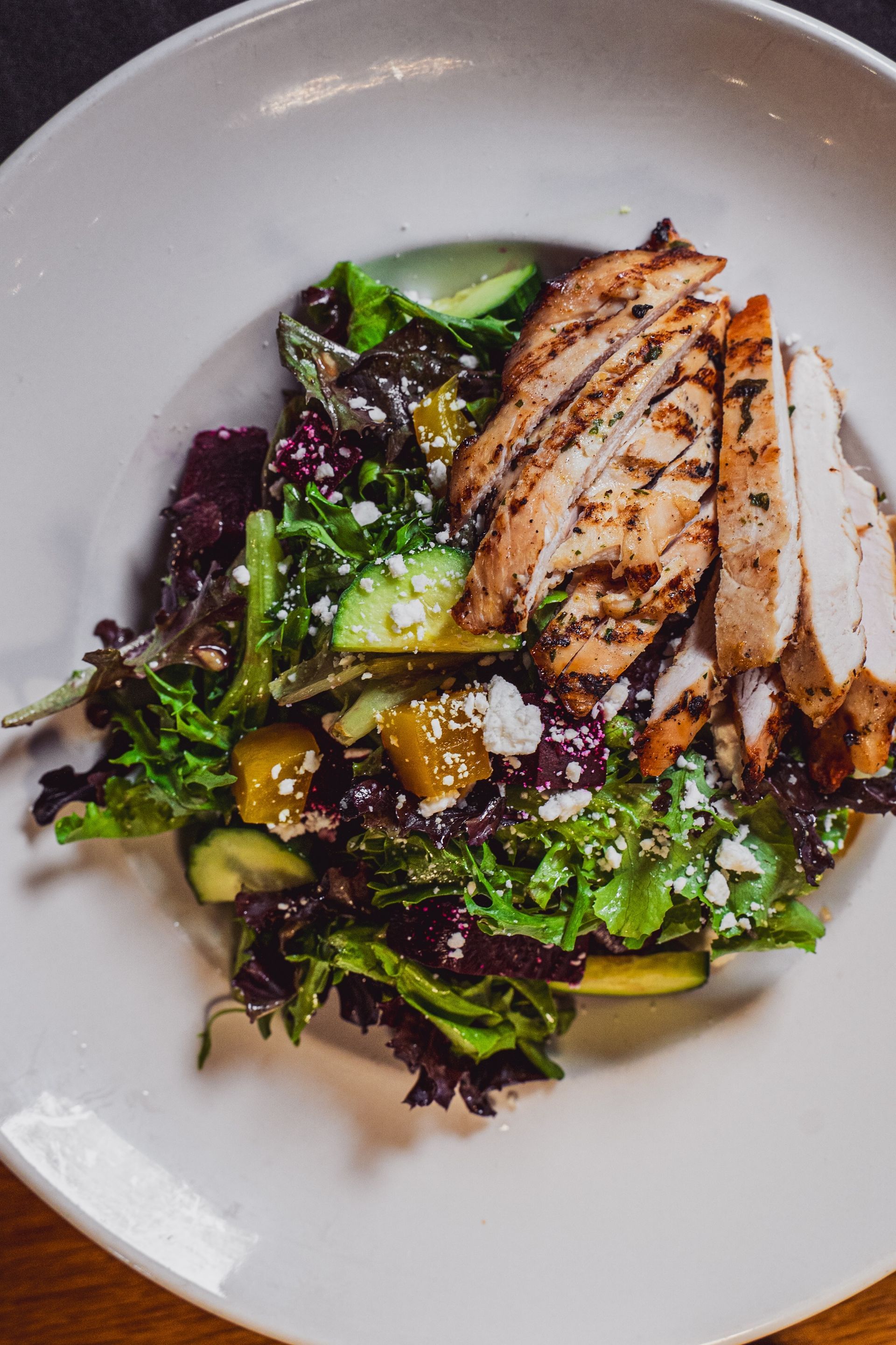 Grilled chicken slices on a mixed green salad with vinaigrette in a white bowl