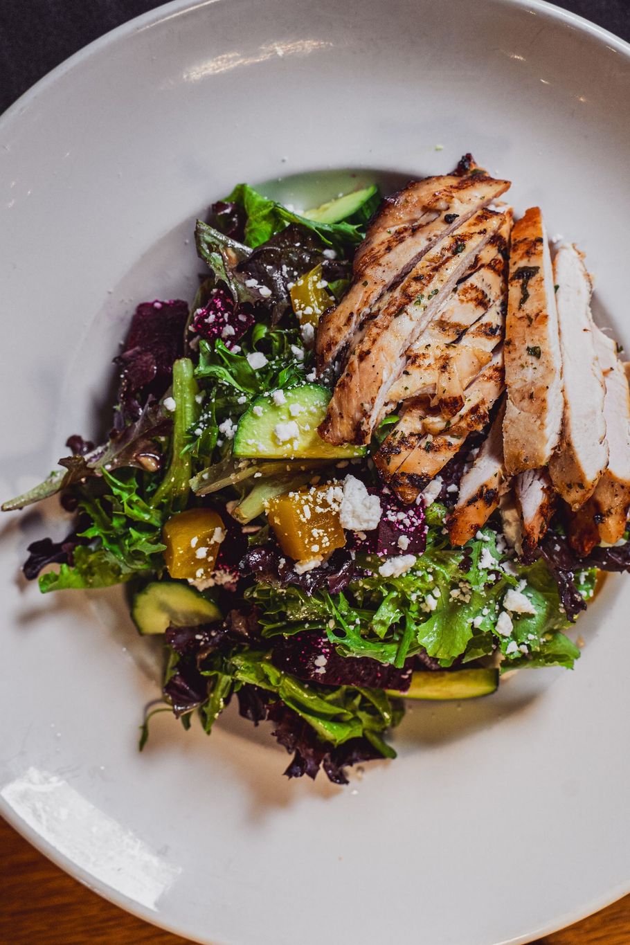 Grilled chicken slices on a mixed green salad with vinaigrette in a white bowl