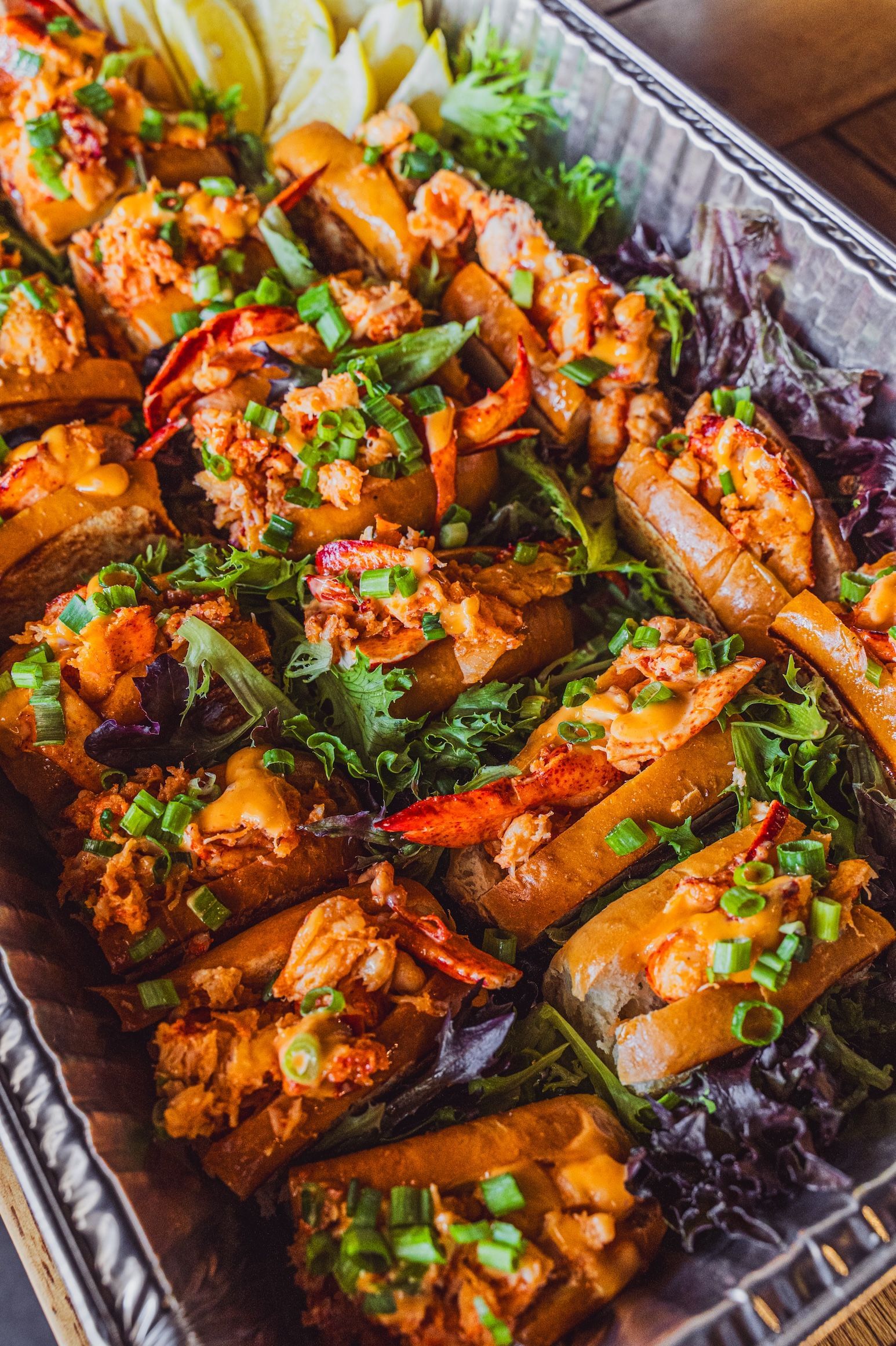 Grilled salmon pieces garnished with herbs on a tray, with lemon wedges and greens.