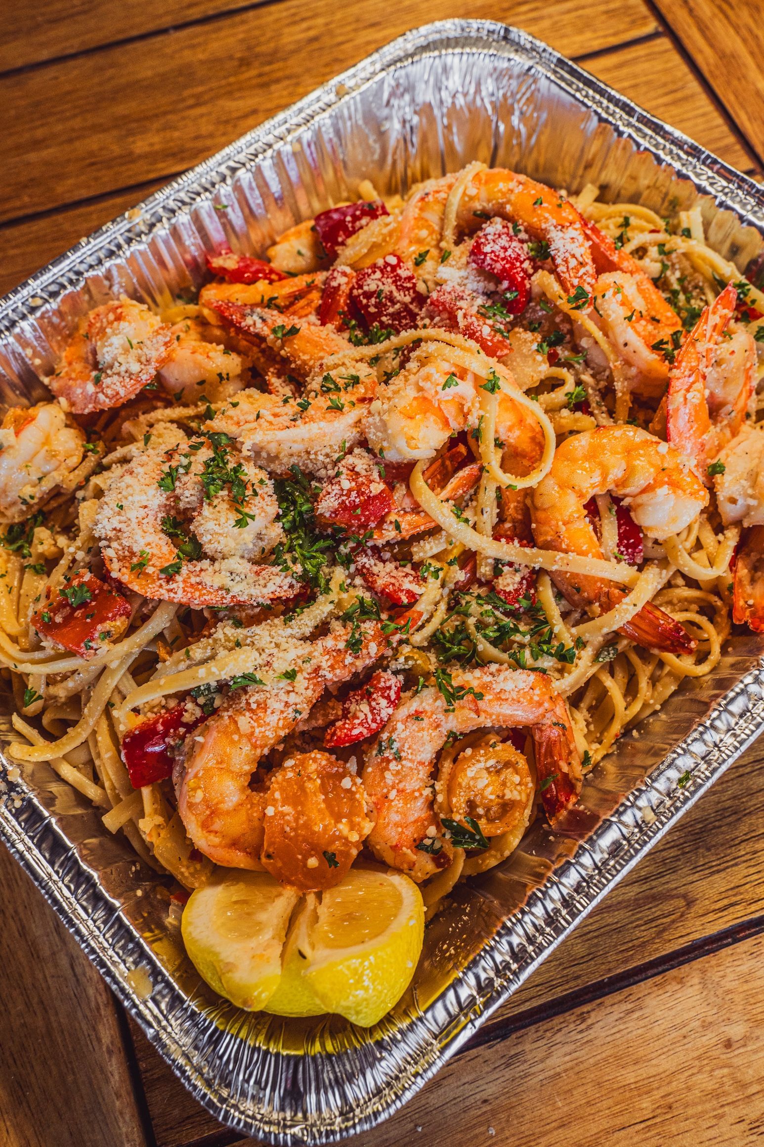 Tray of shrimp pasta with lemon wedges and red peppers on a wooden table