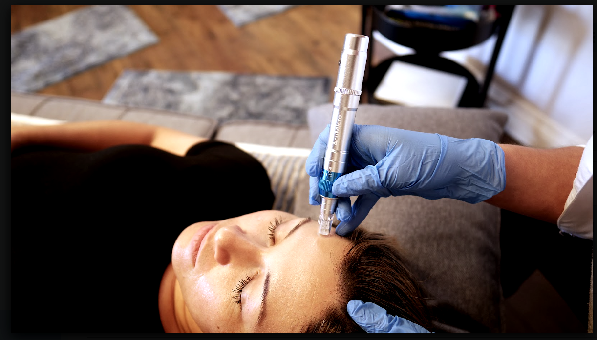 A woman is laying on a couch getting a tattoo on her face.
