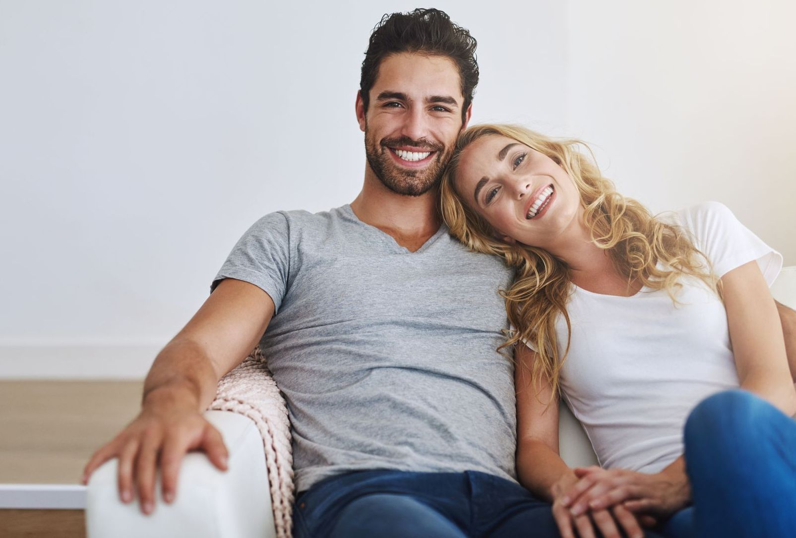 A man and a woman are sitting on a couch holding hands and smiling.