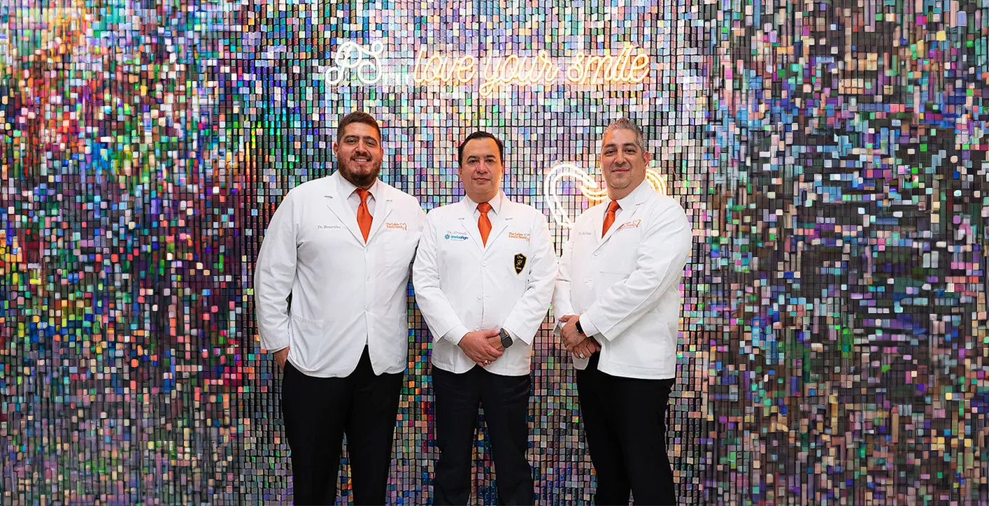 Three men in white coats and orange ties are standing in front of a colorful wall.