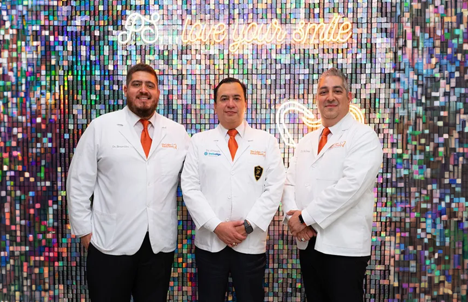 Three men in white coats and ties are posing for a picture in front of a wall.