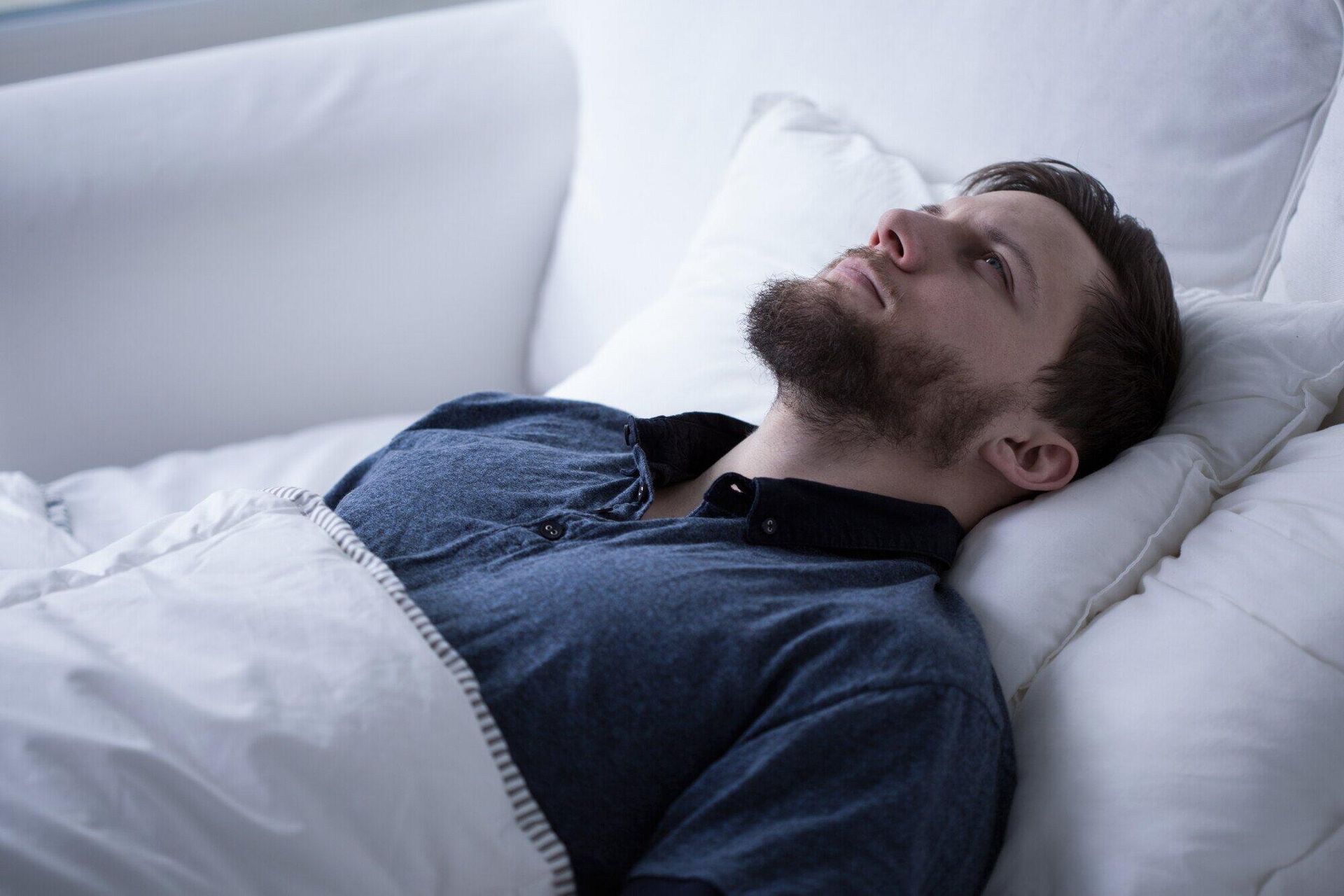 Man lying in bed, eyes closed, looking up, wearing a blue shirt.