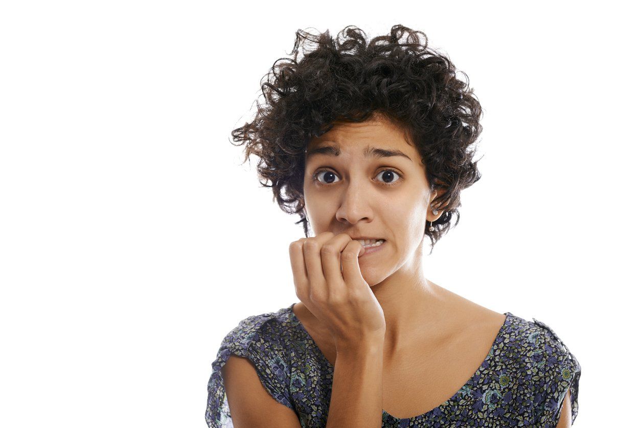 A woman with curly hair is biting her nails.
