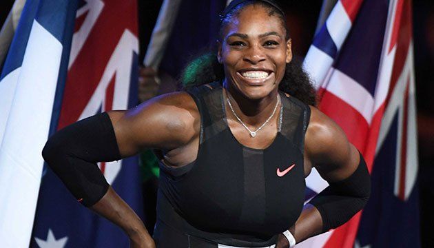A woman in a black tank top is smiling in front of flags.