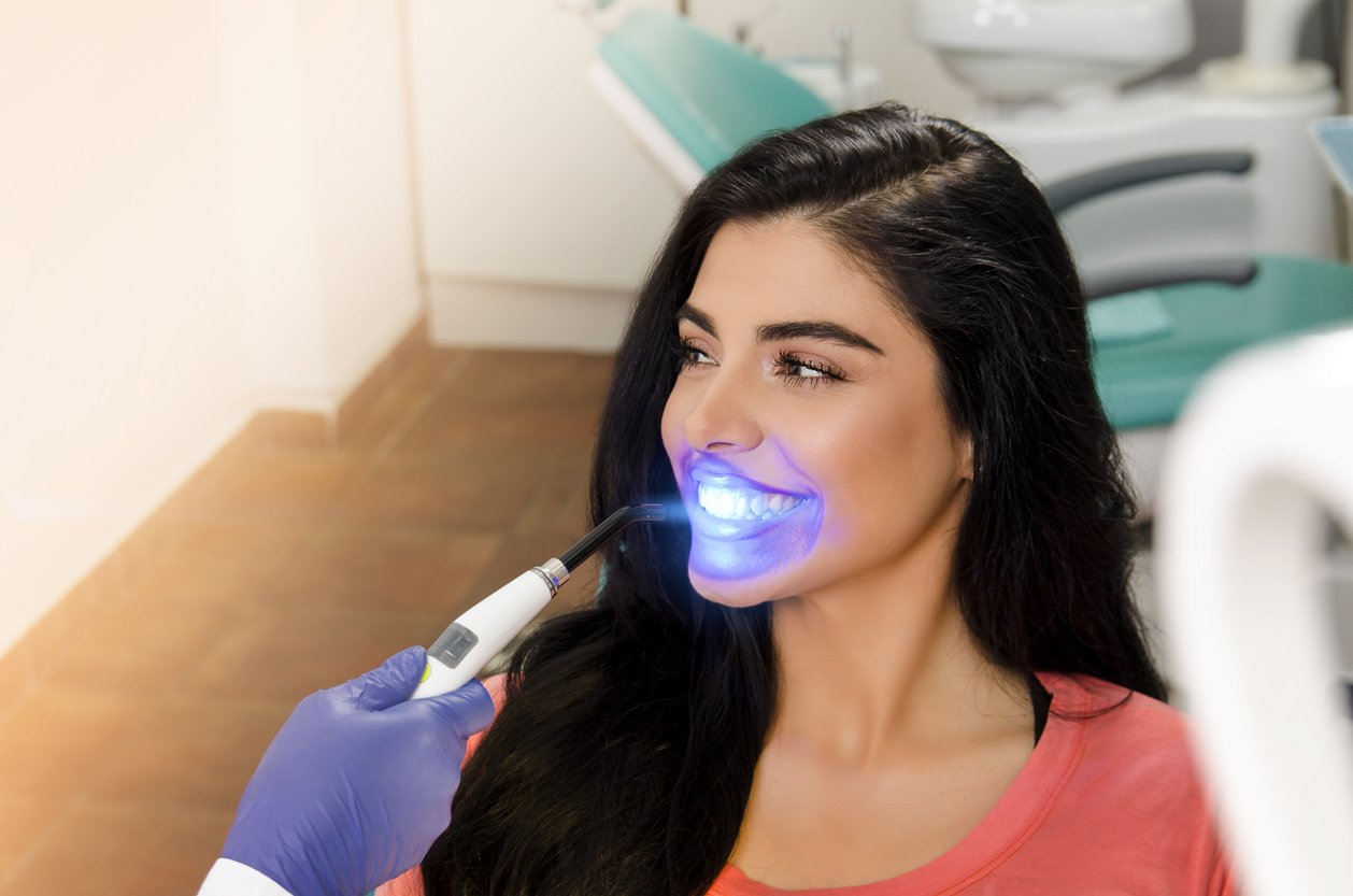 A woman is getting her teeth whitened by a dentist.