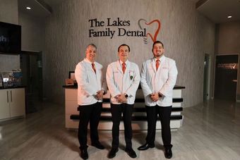 Three dentists are posing for a picture in front of a dental office.