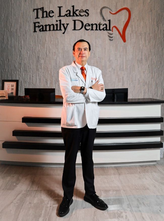 A man in a lab coat is standing in front of a dental office.