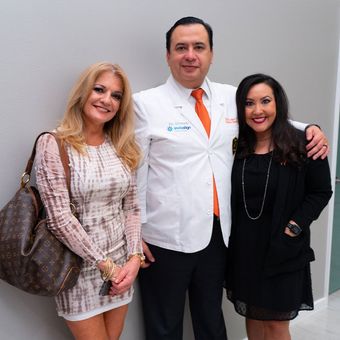 A man in a white coat and tie poses with two women