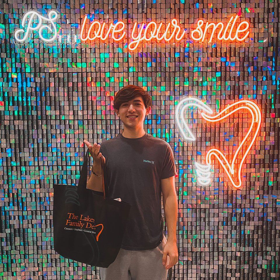 A man is standing in front of a wall with a neon sign that says `` i love your smile ''.