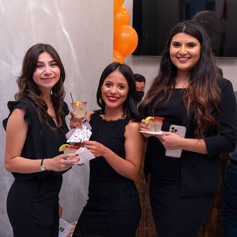 Three women are posing for a picture while holding drinks