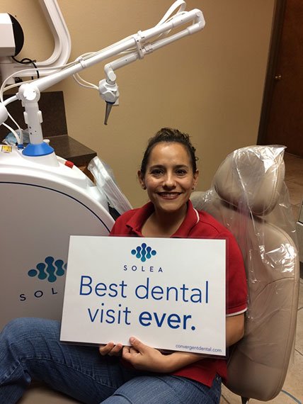 A woman sitting in a dental chair holding a sign that says best dental visit ever