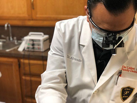 A dentist wearing a white coat and mask is working on a patient 's teeth.