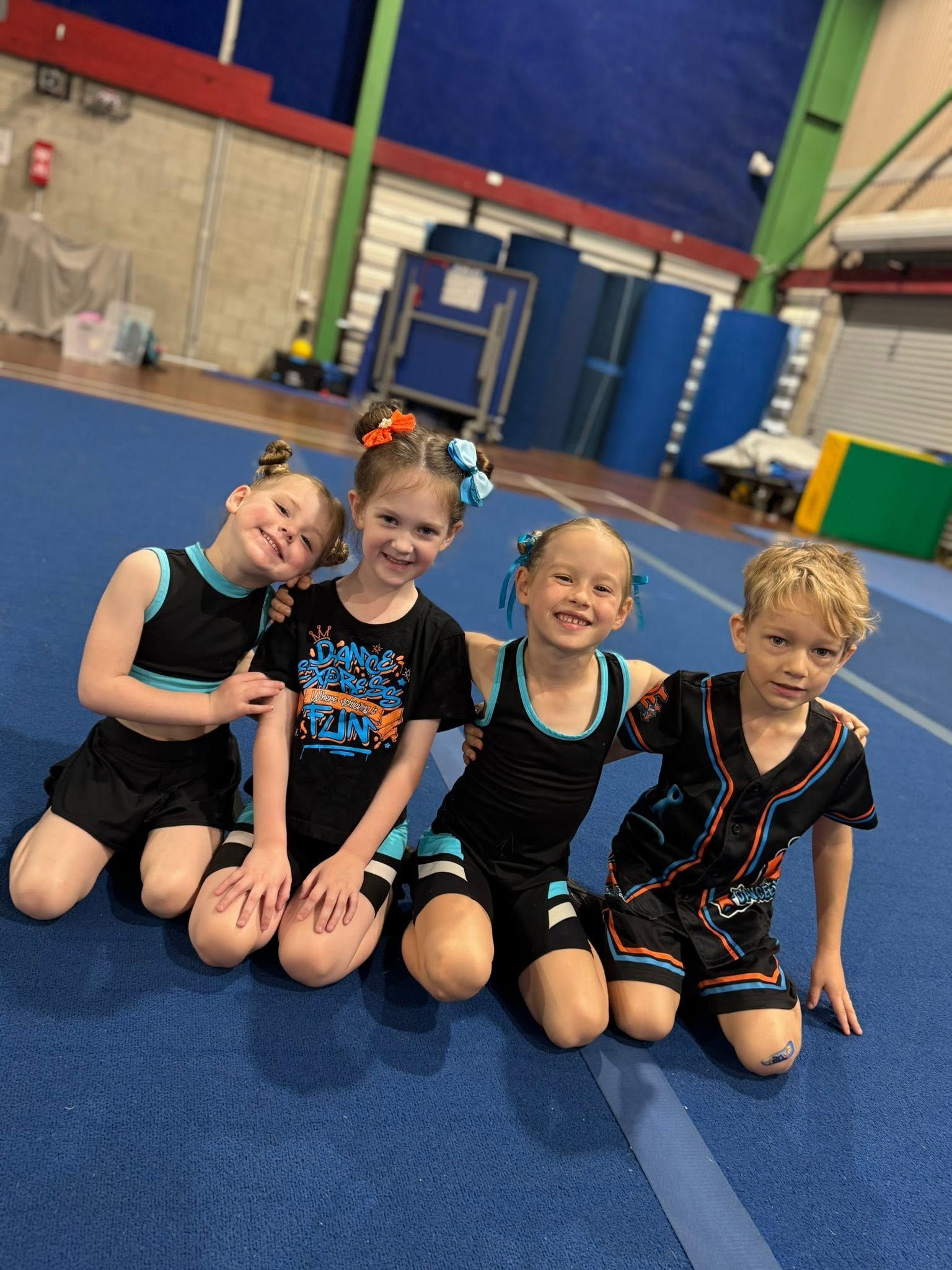 Four Smiling Children in Black Outfits Pose Kneeling — Dance Express Mackay In North Mackay, QLD