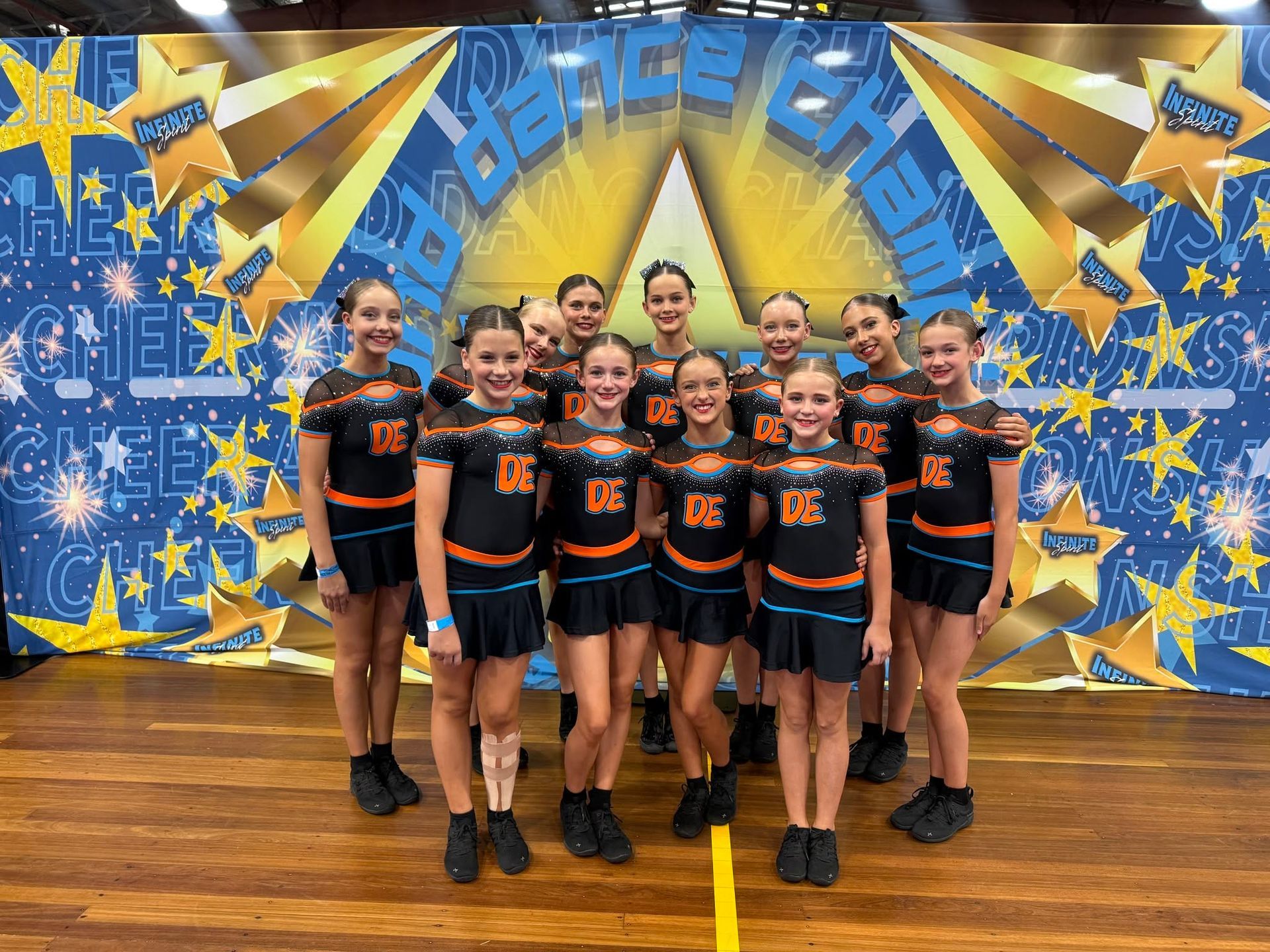 Group of Cheerleaders in Black and Orange Uniforms Posing in Front — Dance Express Mackay In North Mackay, QLD