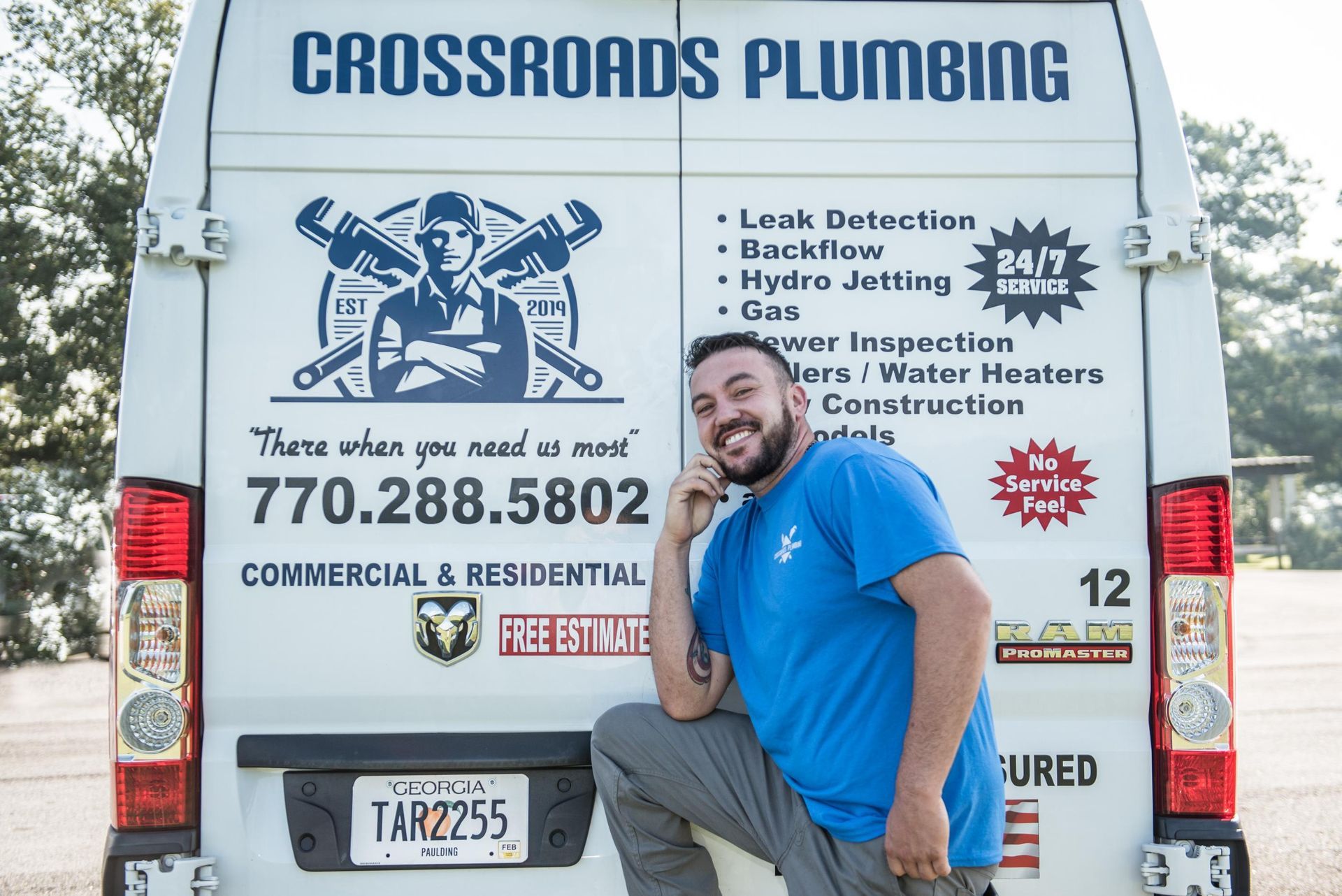 A man is kneeling in front of a crossroads plumbing van.