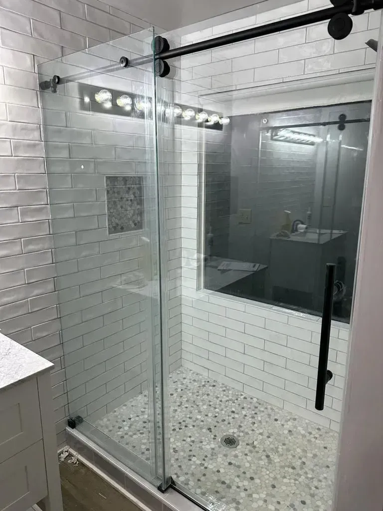Shower with glass door, black hardware, white subway tile walls, and mosaic tile floor.