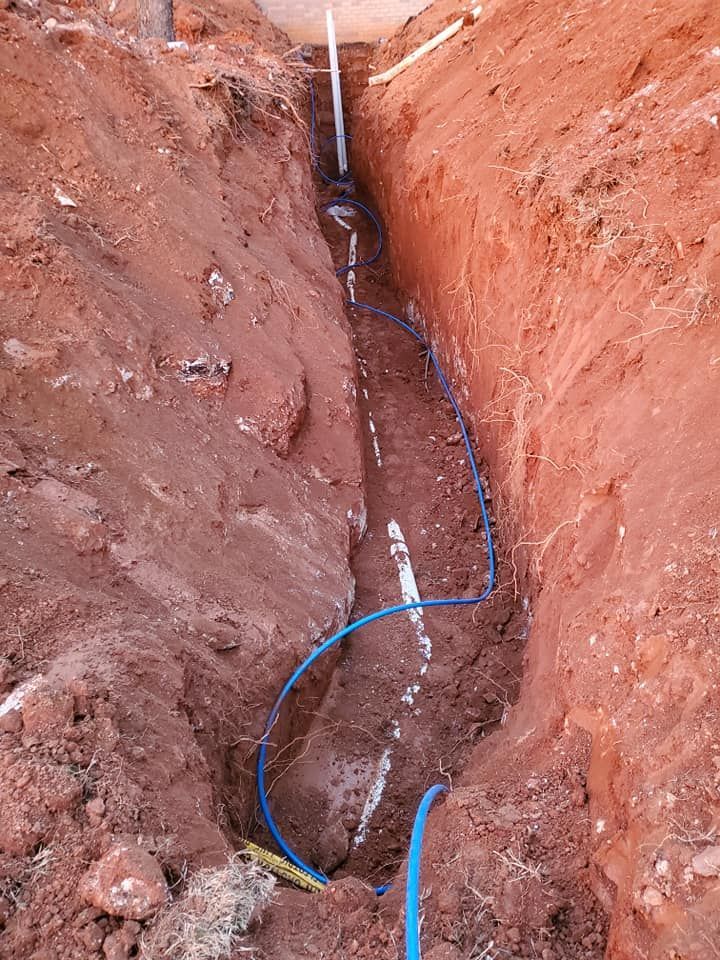A blue hose is laying in the dirt next to a pipe.