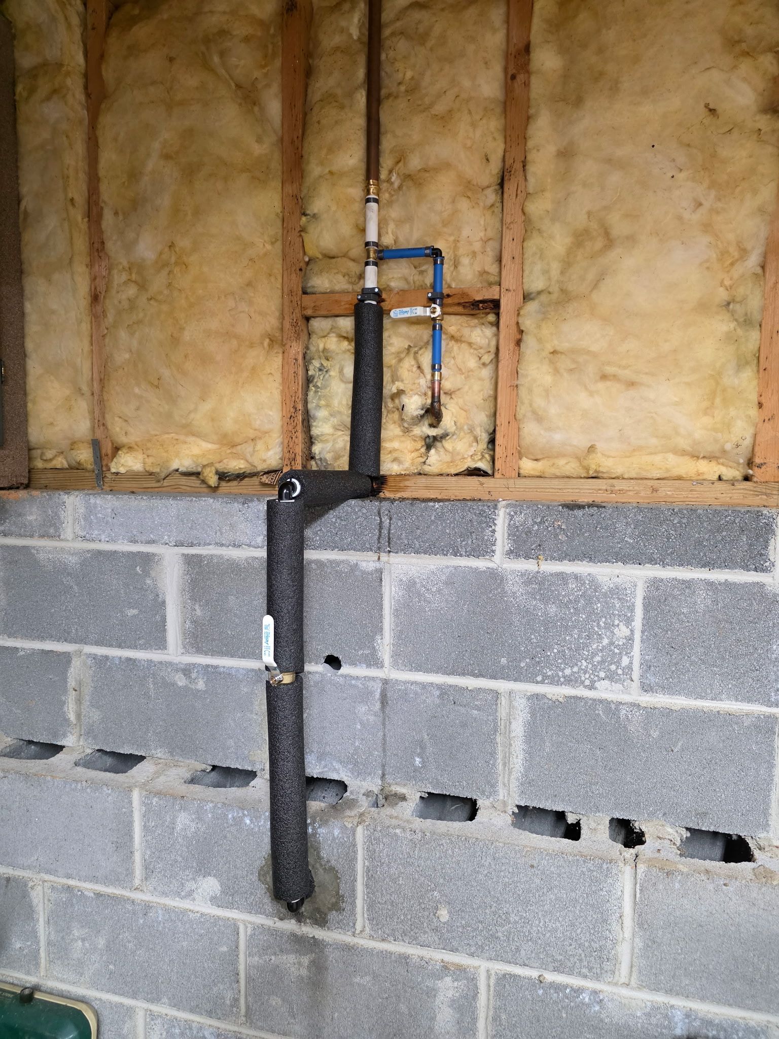 Basement wall with exposed insulation, cinder blocks, and a vertical pipe assembly