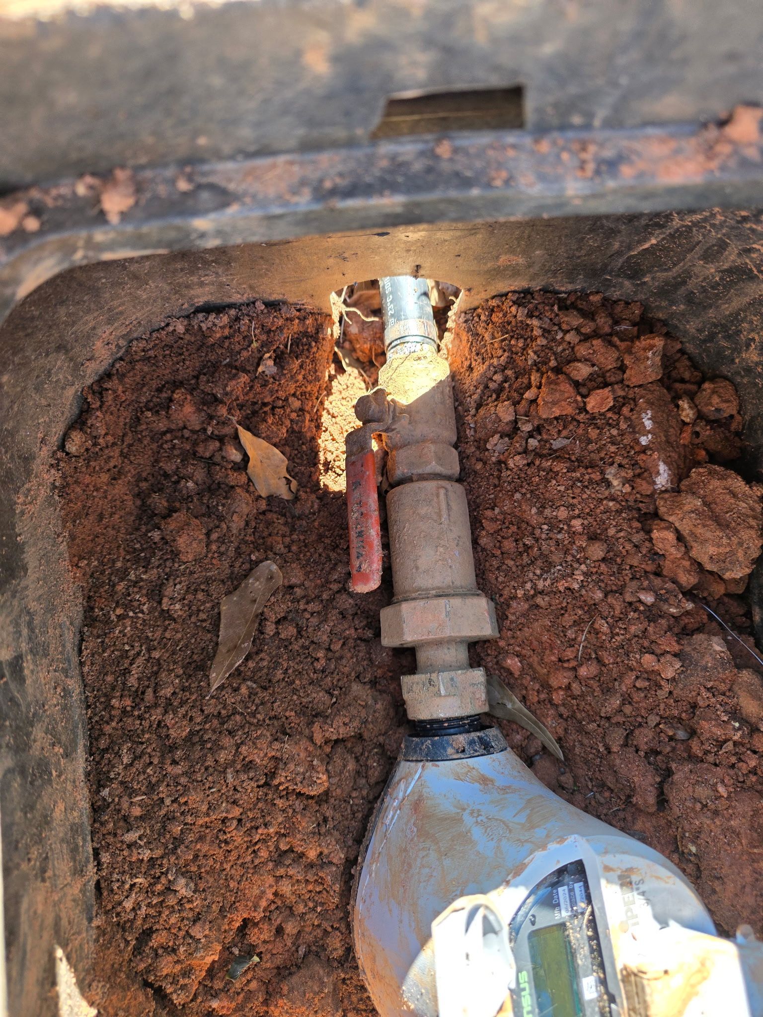 Rusty pipe and valve inside a corroded metal box, with sunlight reflecting off the fitting.