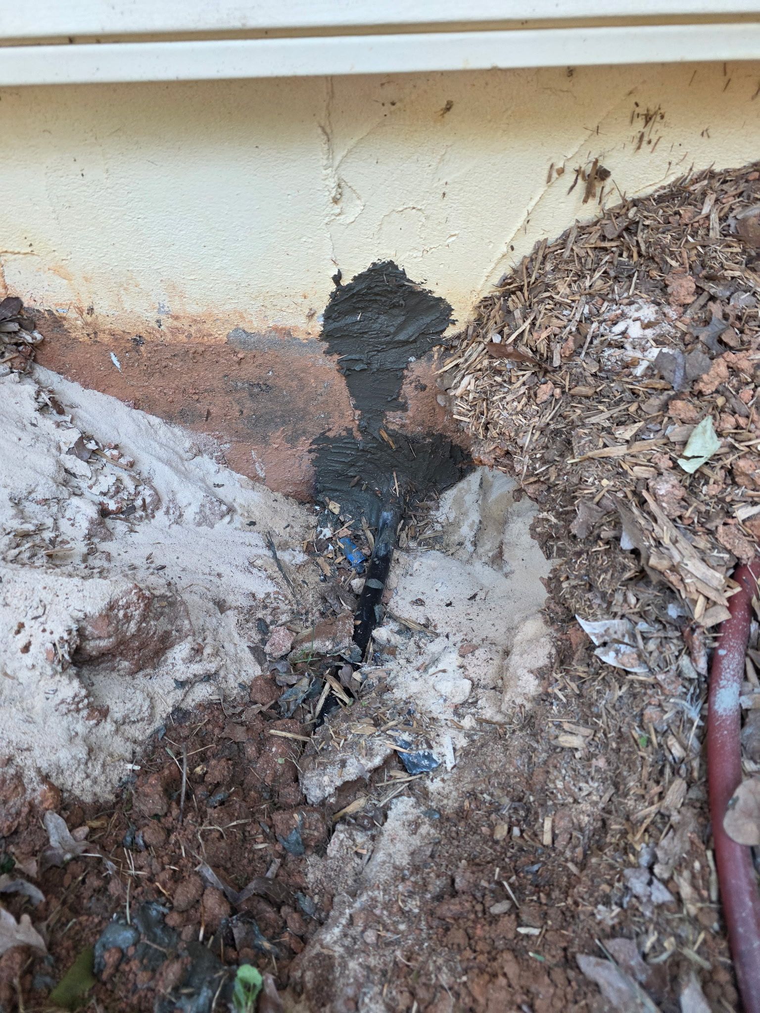 Cracked basement wall with a hole, damp soil, debris, and a red hose along the right side.