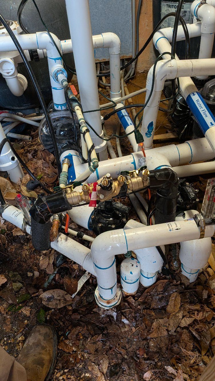 White PVC pipes and valves tangled in muddy ground, with a damaged pipe section leaking debris.