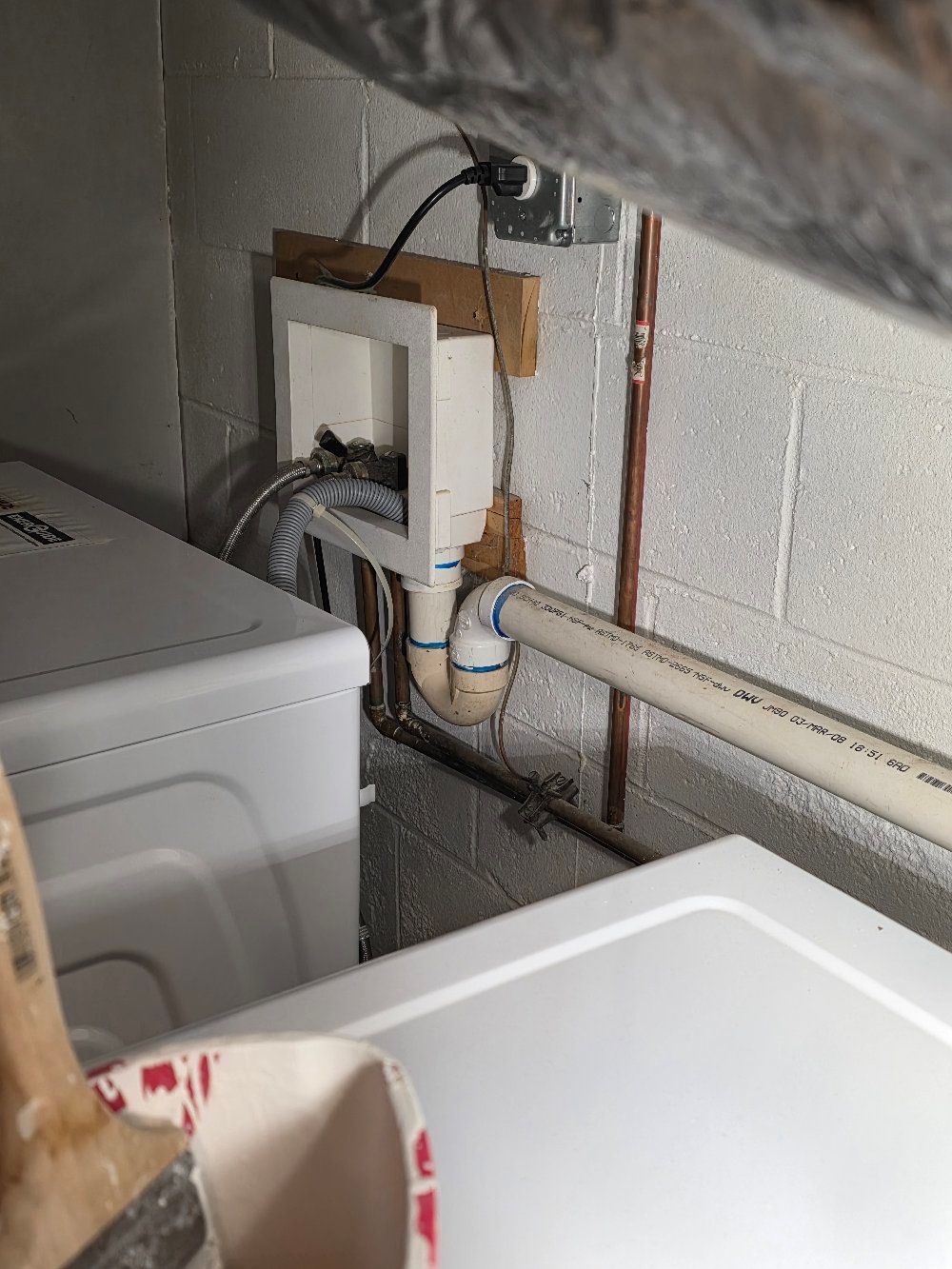 Laundry room wall with exposed plumbing and wiring beside a washing machine.
