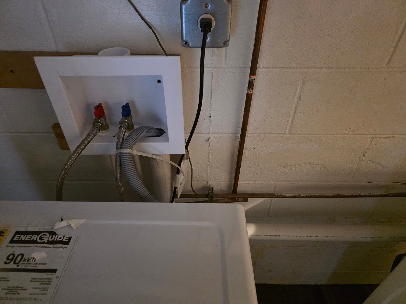 Laundry hookups and wall outlet above a washing machine in a basement laundry area
