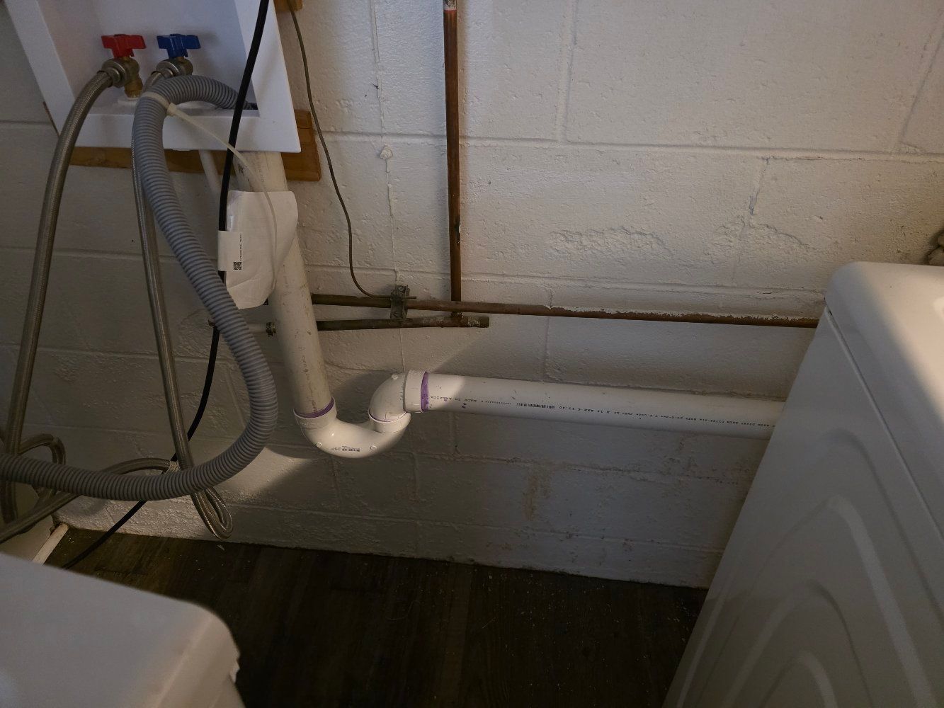 Laundry room plumbing with white drain pipes and hoses along a wall near a washing machine