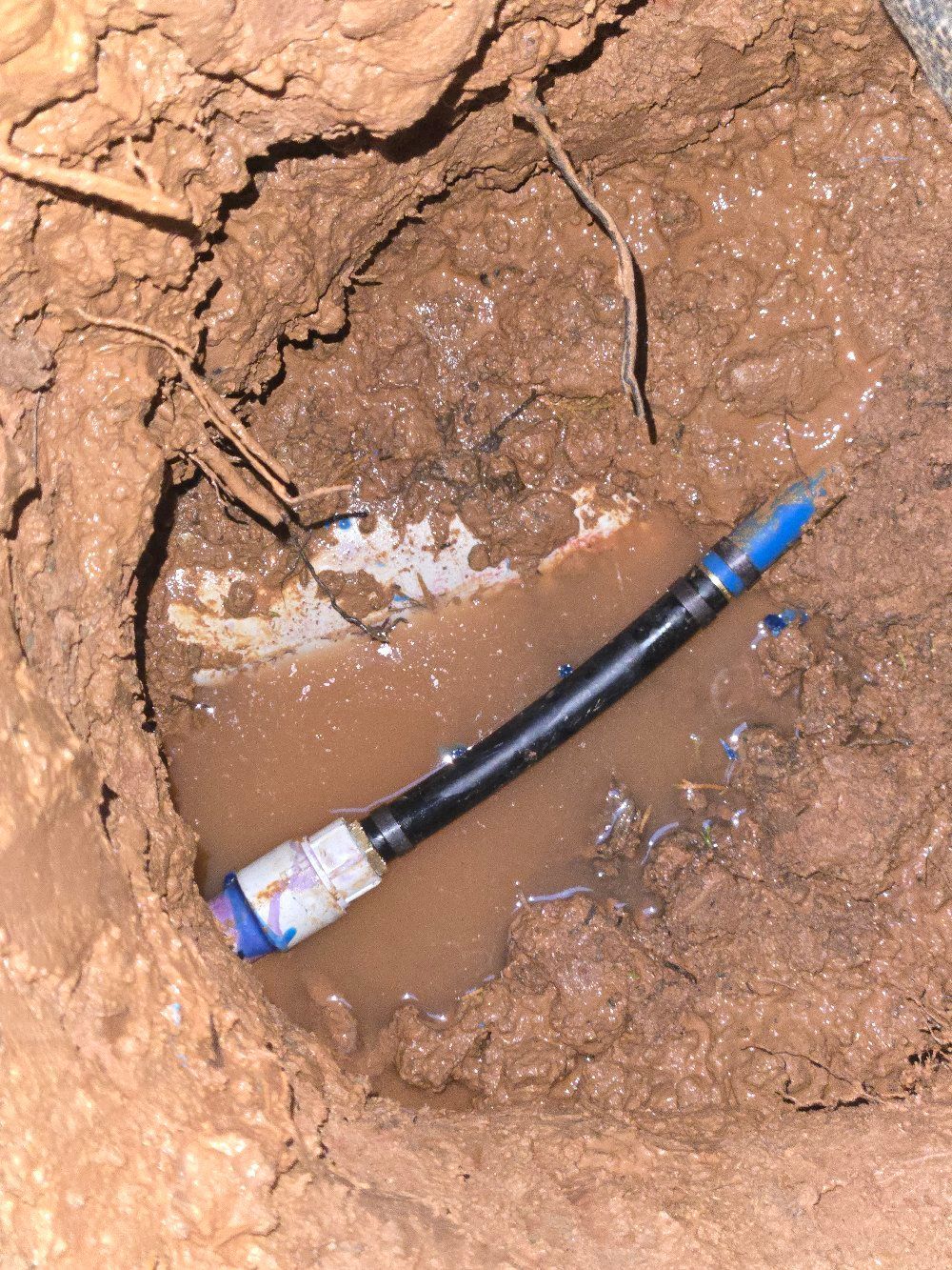 Damaged black cable with blue end lying in a muddy hole in cracked dirt