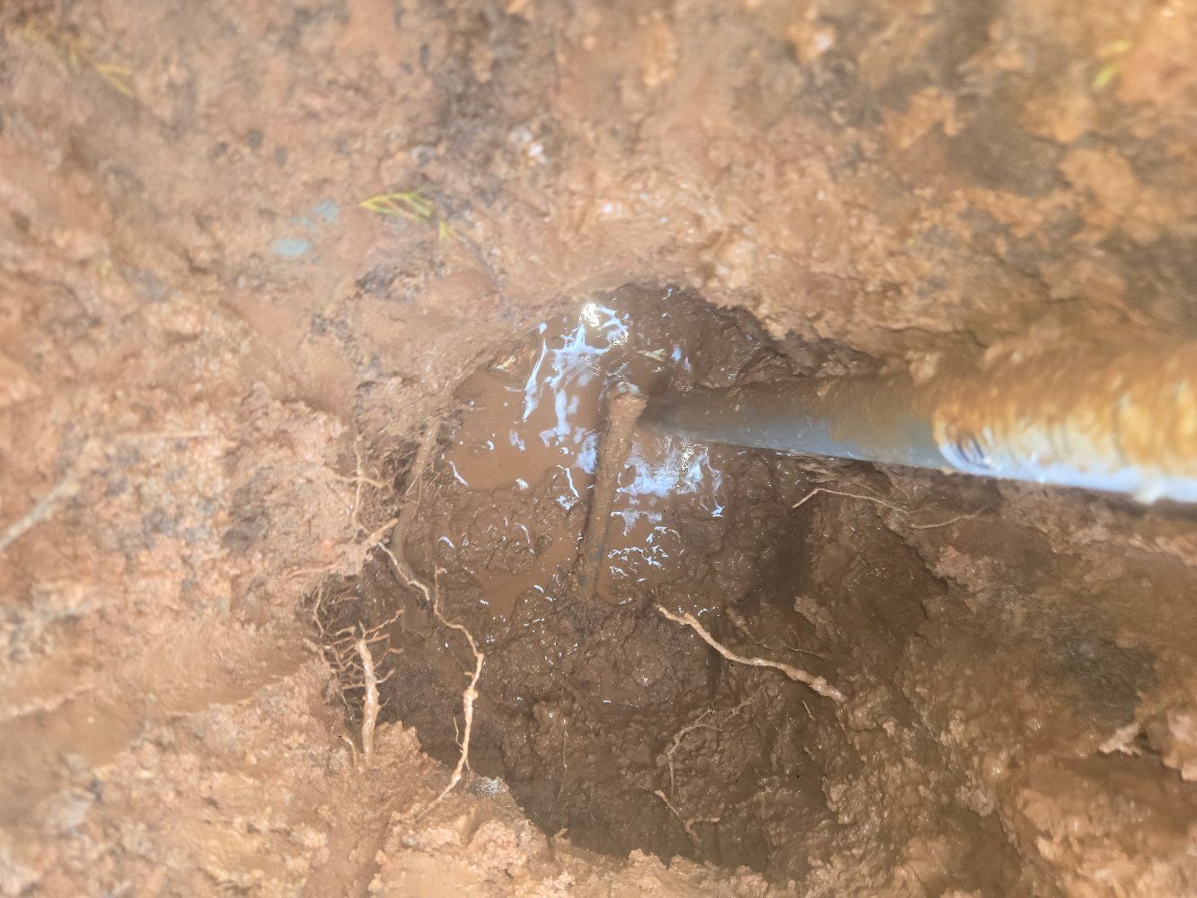 Close-up of muddy ground with a small water-filled hole and a tool touching the edge