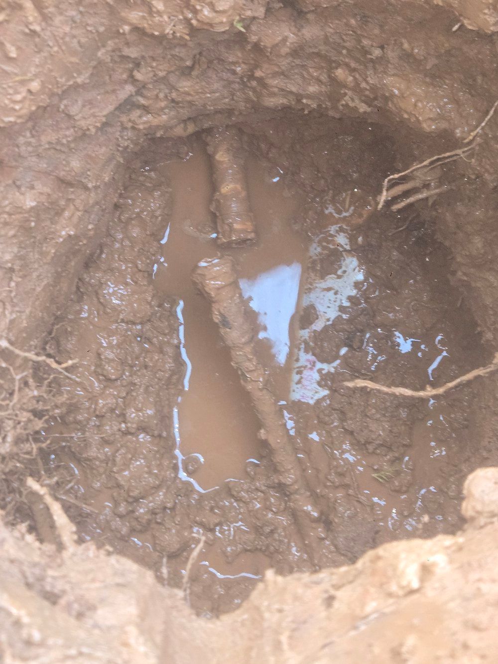 Close-up of muddy ground with a shallow puddle and exposed pipe or root in a small hole