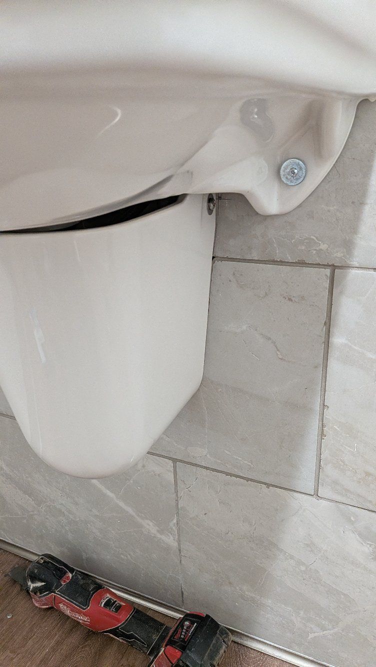 Close-up of a white urinal and gray tiled bathroom floor, with a red power tool at the bottom edge.