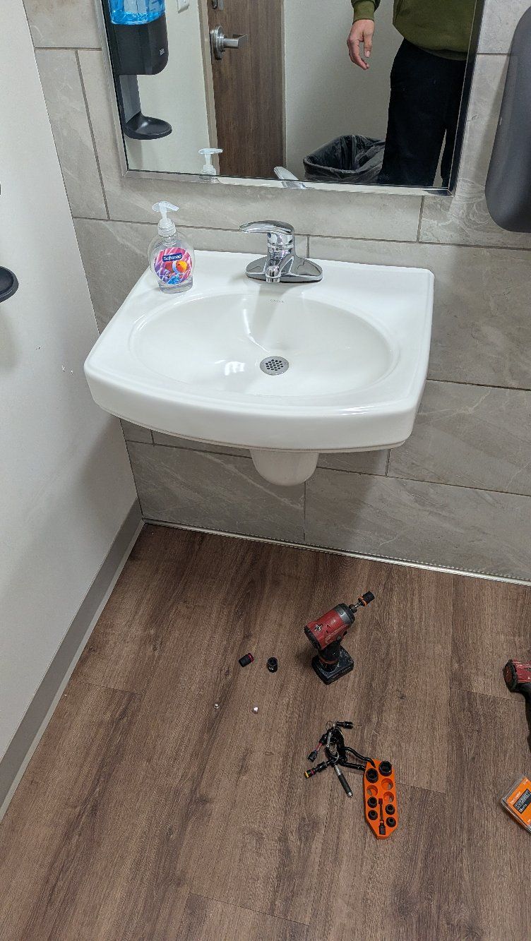 Small bathroom sink with mirror, soap dispenser, and toy cars scattered on the wood floor.