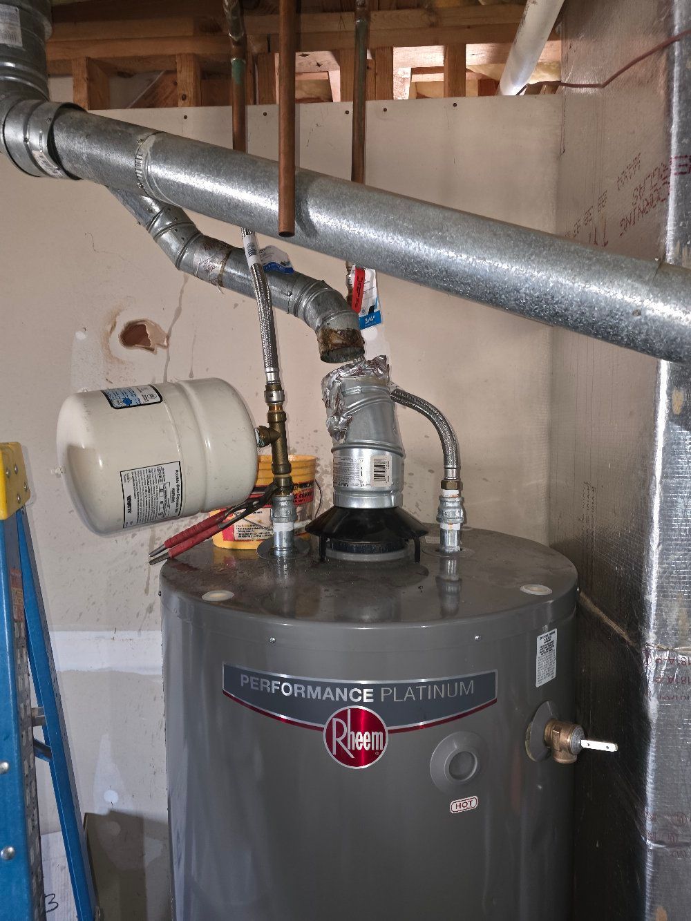 Water heater with metal ducting and vent pipes in a basement utility room.