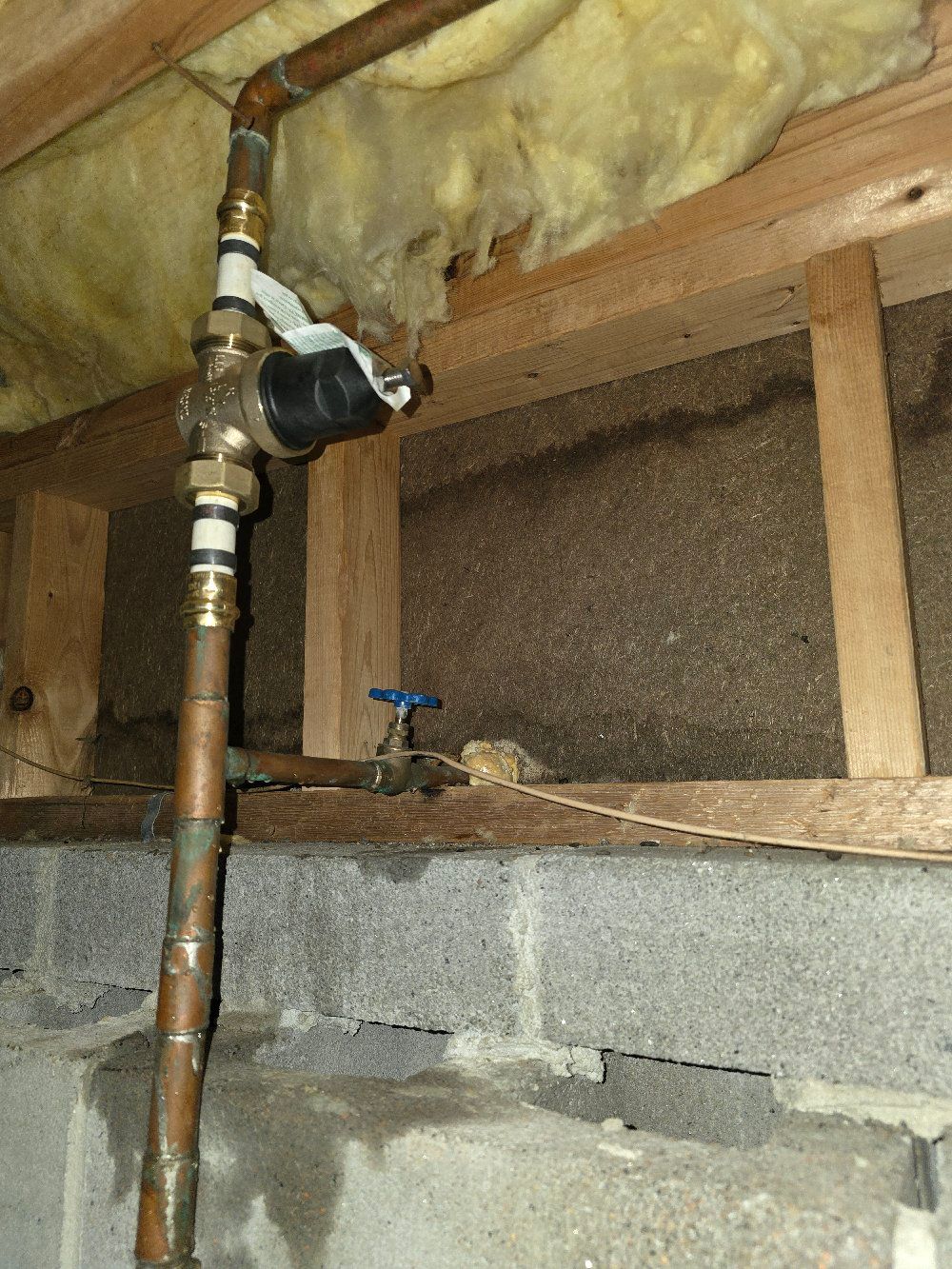 Copper pipe and valve assembly in a basement beside exposed insulation and cinderblock wall
