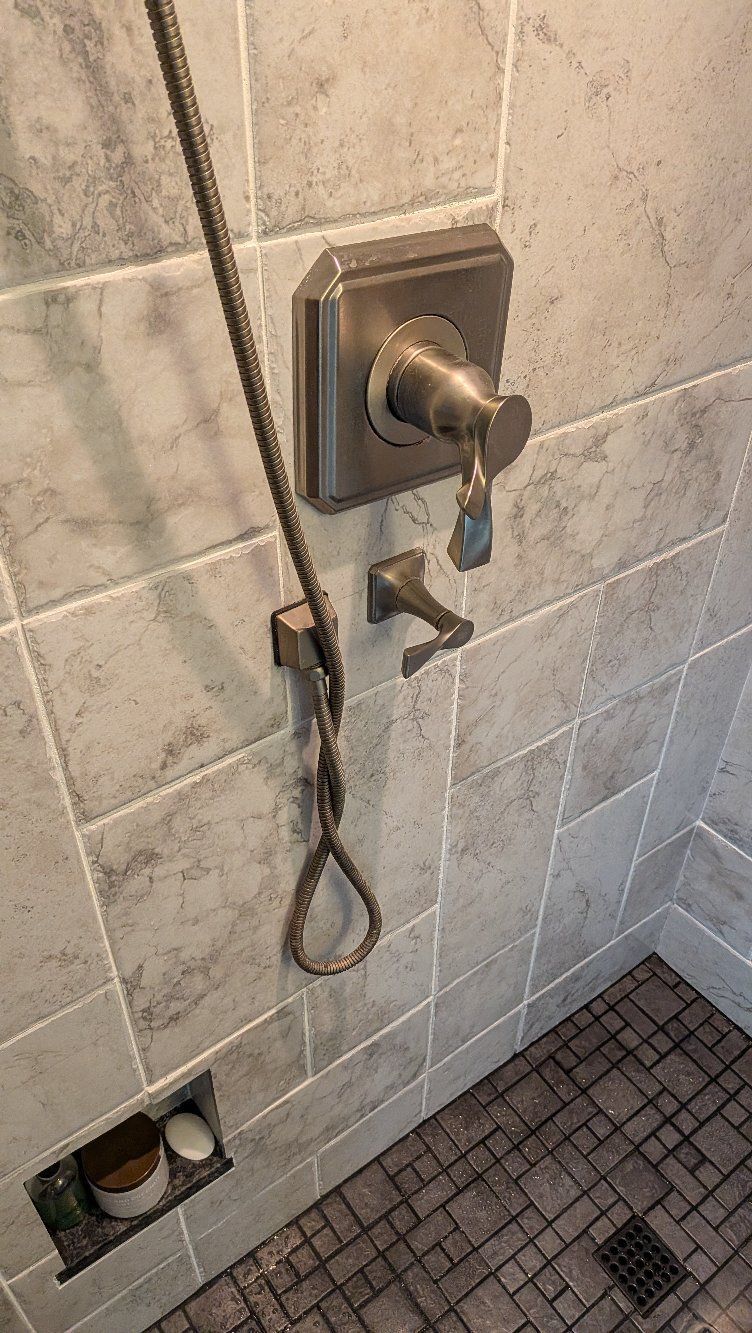 Tile shower with handheld sprayer, hose, soap dish, and floor drain.