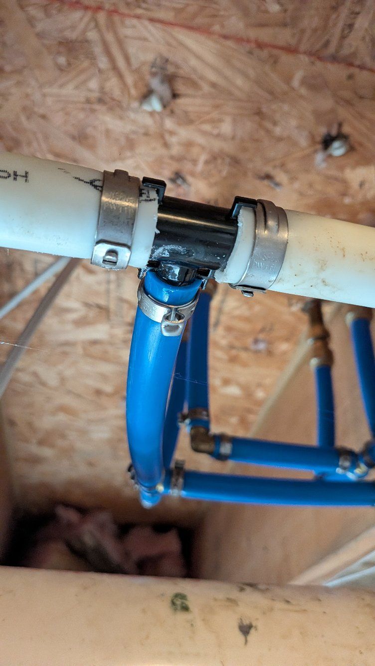 Blue and white pipes joined with a black connector beneath a wooden floor joist