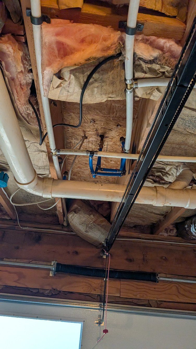 Exposed ceiling pipes and ductwork in an unfinished basement with insulation and wooden joists