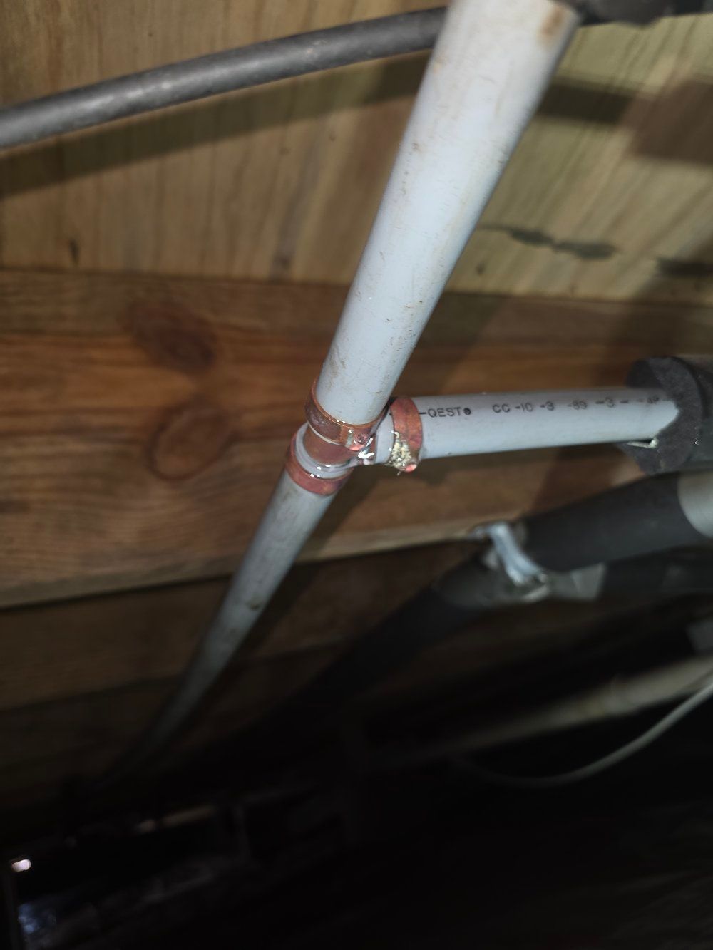 Red and white PVC pipes connected under a wooden floor with a metal support bar visible.