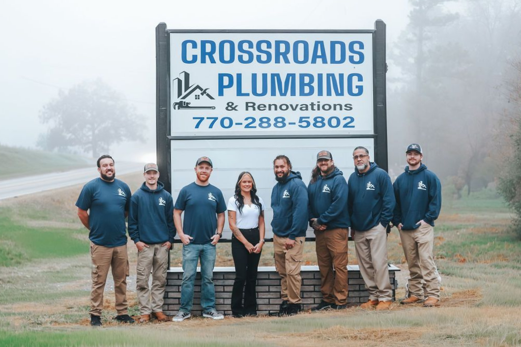 A man is kneeling in front of a crossroads plumbing van.