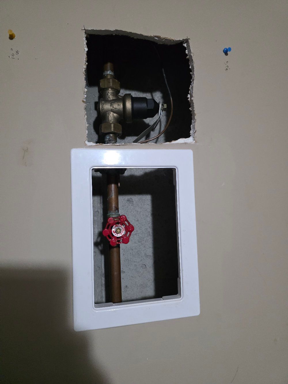 Wall with two exposed plumbing valves, one brass fitting above and a red shutoff valve below.