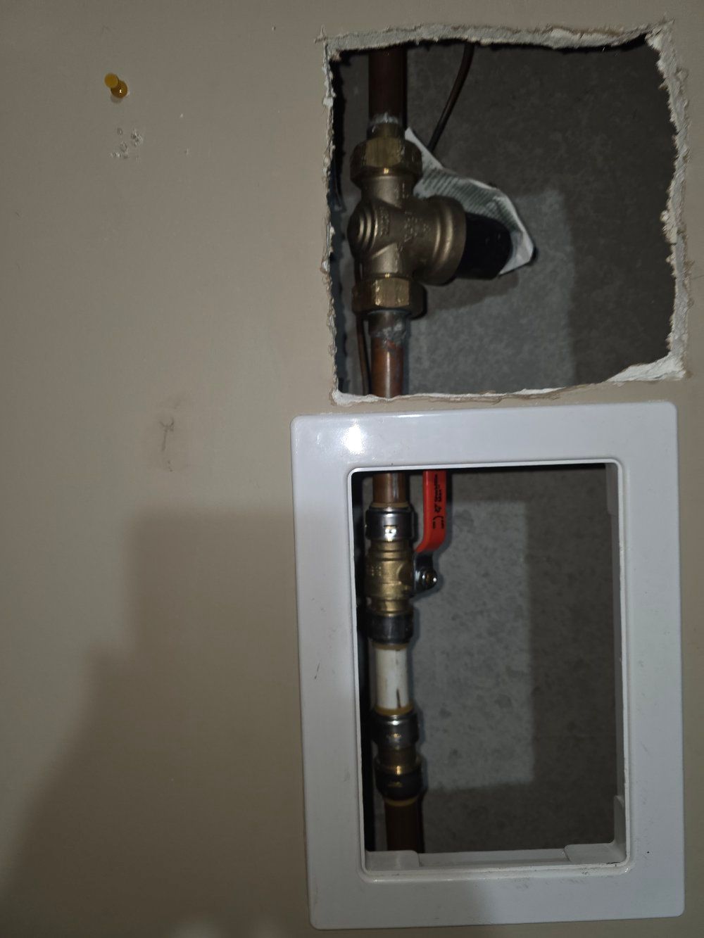 Exposed plumbing valves and copper pipes inside two wall openings during repair work