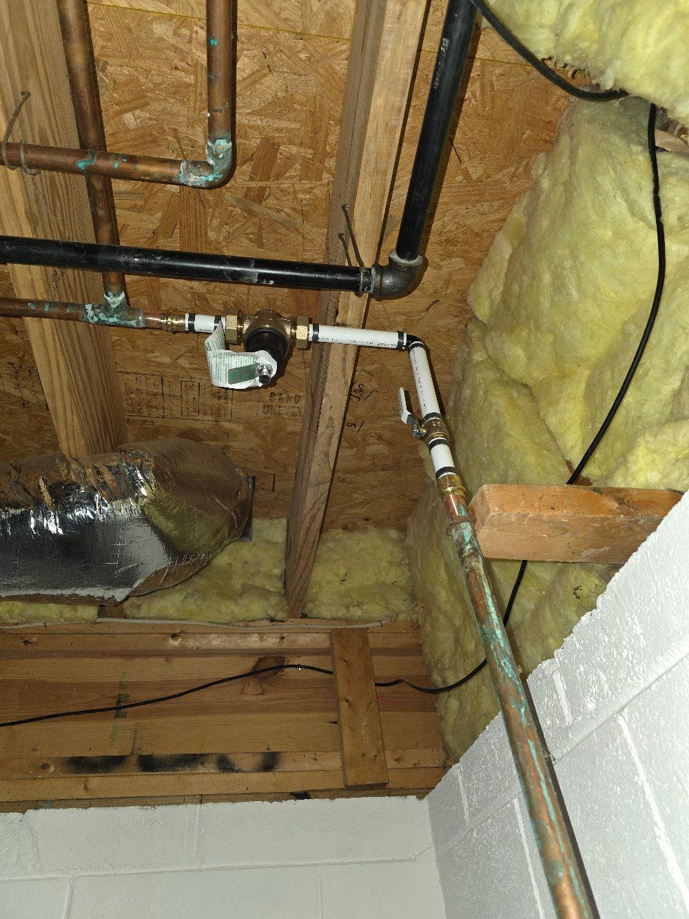 Exposed plumbing pipes and insulation in an unfinished basement ceiling above cinder block walls