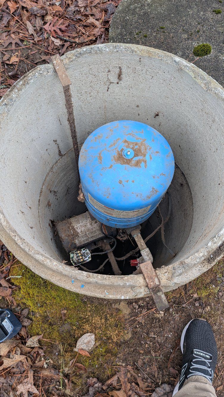Blue utility valve inside a concrete access pit with pipes and debris around it